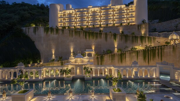 A large, multi-story hotel with a pool area in the foreground, featuring a tiled floor and several lounge chairs. - Aurika, Udaipur - Luxury by Lemon Tree Hotels (Udaipur)