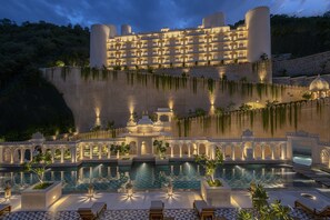 A large, multi-story hotel with a pool area in the foreground, featuring a tiled floor and several lounge chairs. - Aurika, Udaipur - Luxury by Lemon Tree Hotels (Udaipur)
