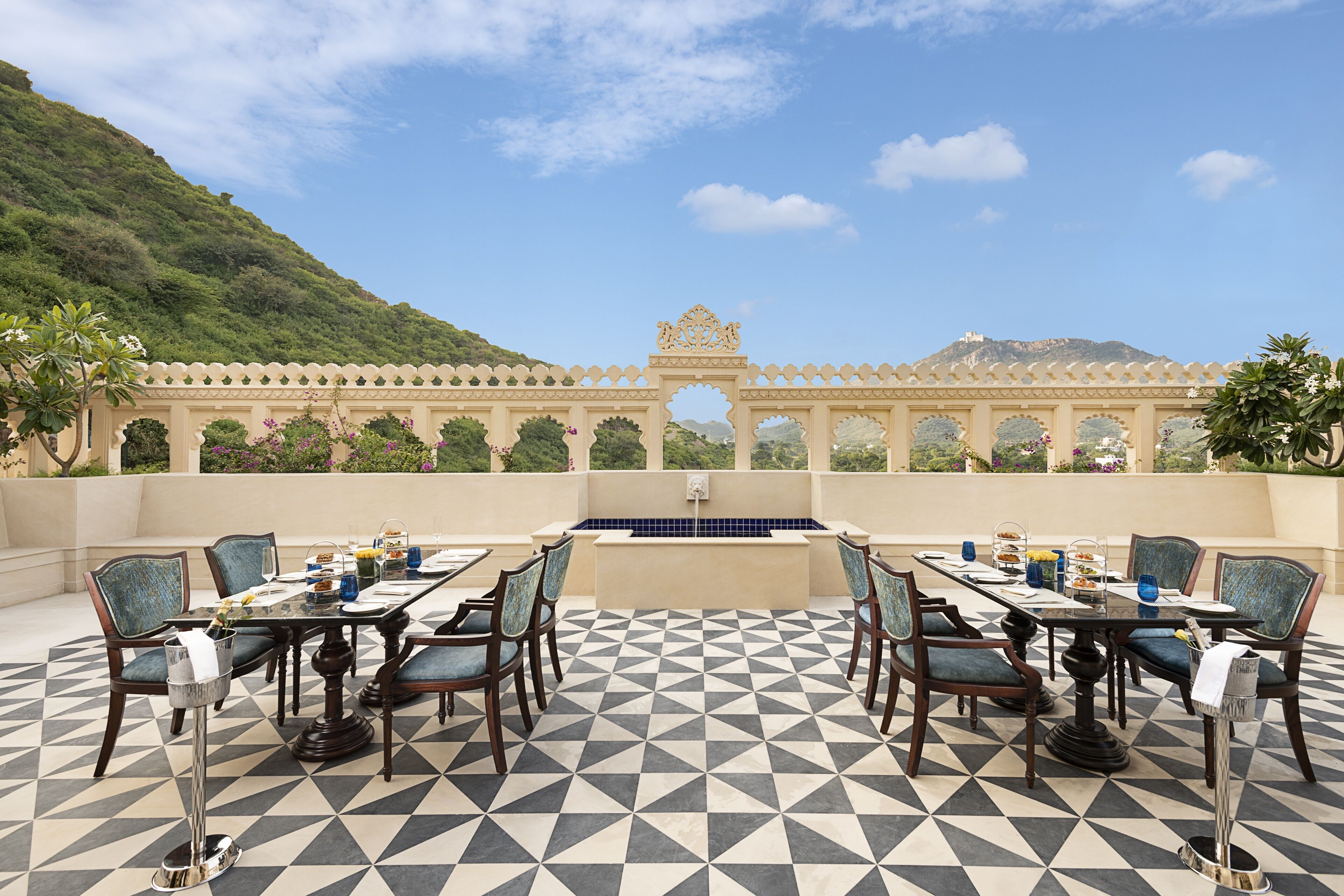 An outdoor dining area with a geometric patterned floor, a central pool, and a view of a mountain.