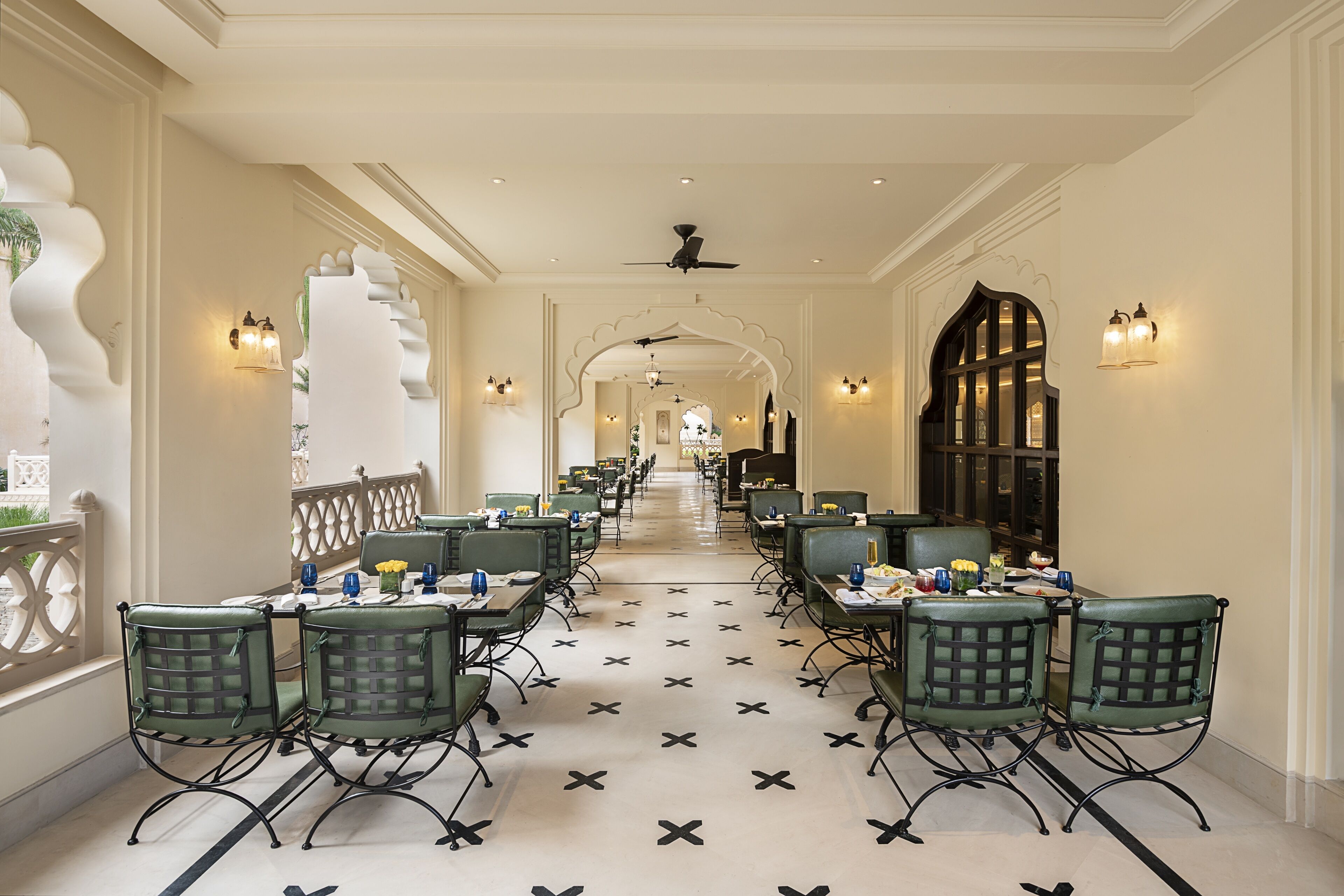 A long corridor with tables and chairs, a patterned floor, and decorative wall sconces.