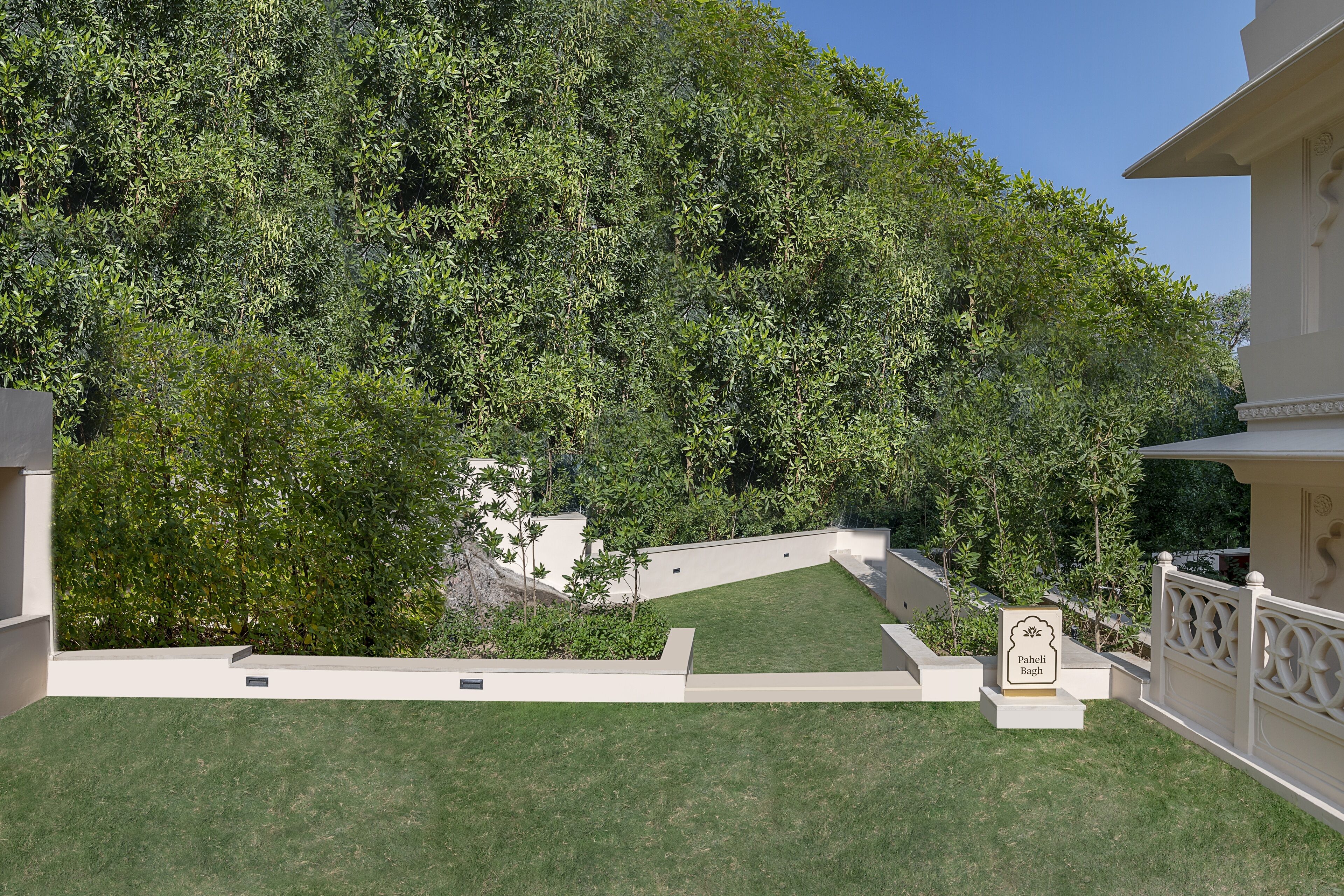 A landscaped garden with a white fence, a sign reading "Pahendi Bagh," and a building with classical architecture.