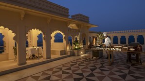 An outdoor dining area with a chef preparing food, surrounded by traditional architecture and a patterned floor. - Aurika, Udaipur - Luxury by Lemon Tree Hotels (Udaipur)