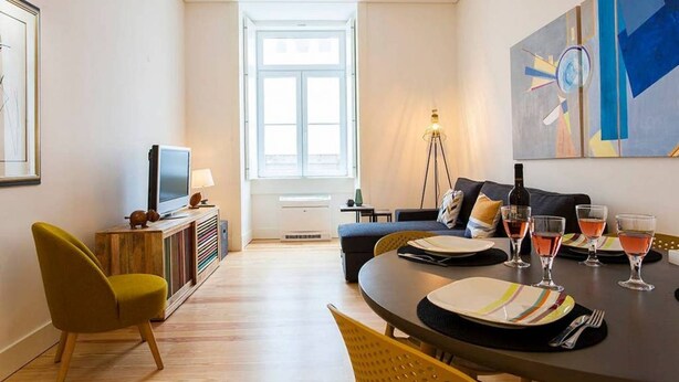 Ein modernes Wohnzimmer mit einer Couch, einem Esstisch für vier Personen und einem Fernseher auf einer Holzkommode.