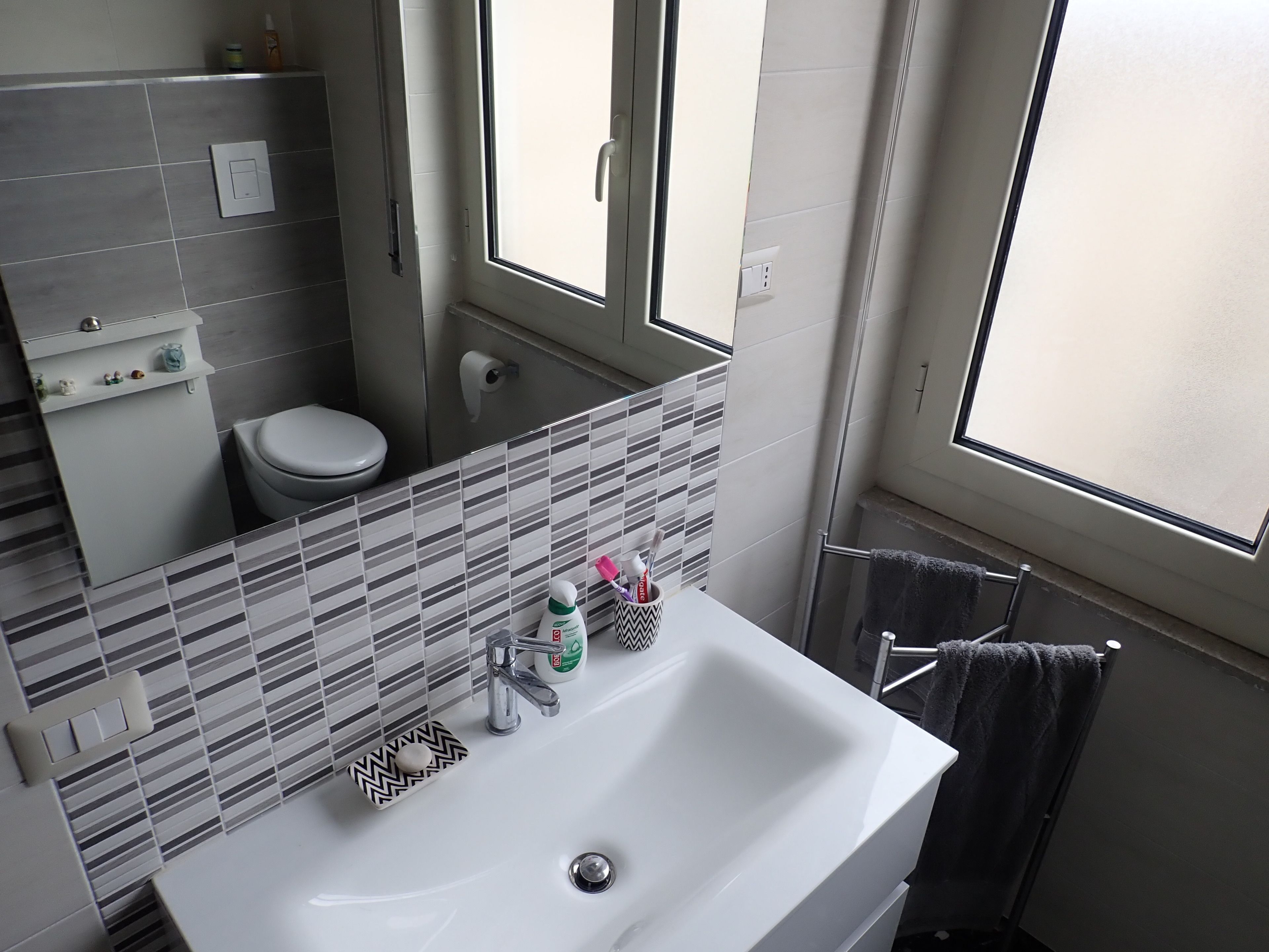 Un bagno con un lavandino bianco, uno specchio, un WC e una finestra.