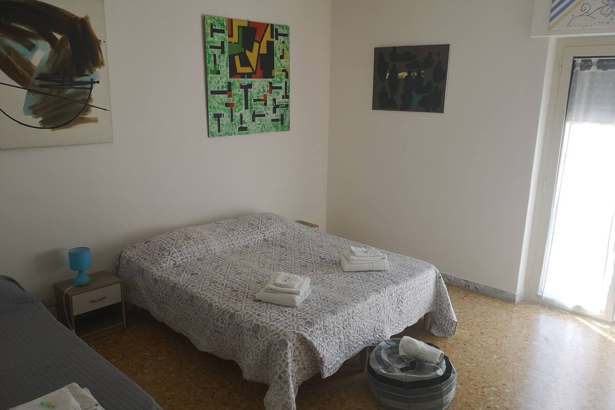 Un dormitorio con cama, mesita de noche, lámpara azul, colcha estampada y una pequeña alfombra.