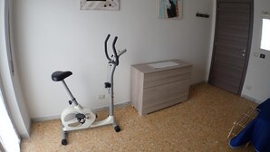 Une pièce comprenant un vélo d’appartement, un petit meuble et une porte.