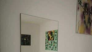 Une chambre d’hôtel avec un grand miroir, un lit recouvert d’une couverture à motifs gris, une petite table de chevet avec un téléphone, un interrupteur fixé au mur et un tableau abstrait encadré.