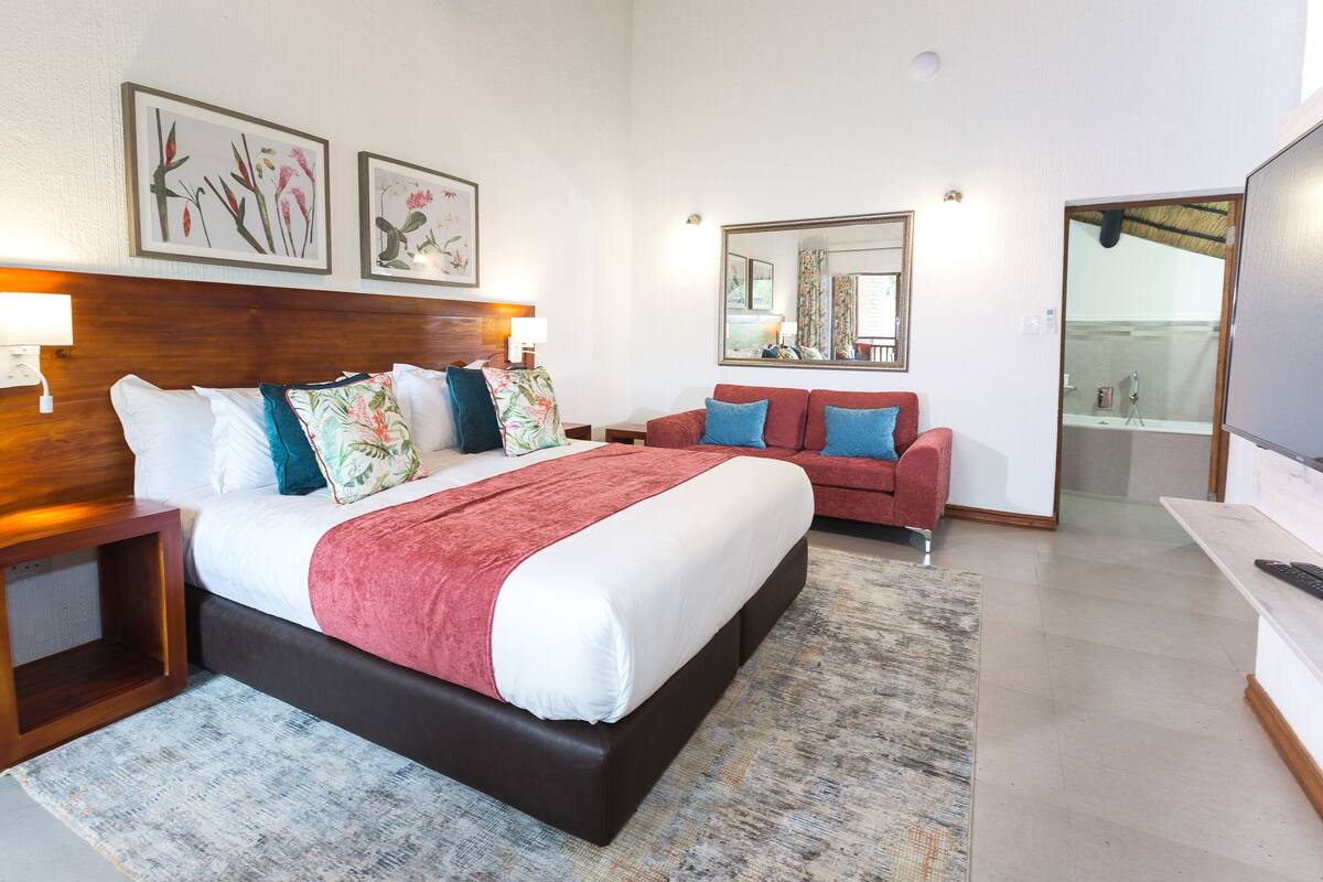 A hotel room with a large bed, a sofa, a desk, and a bathroom visible through an open door.