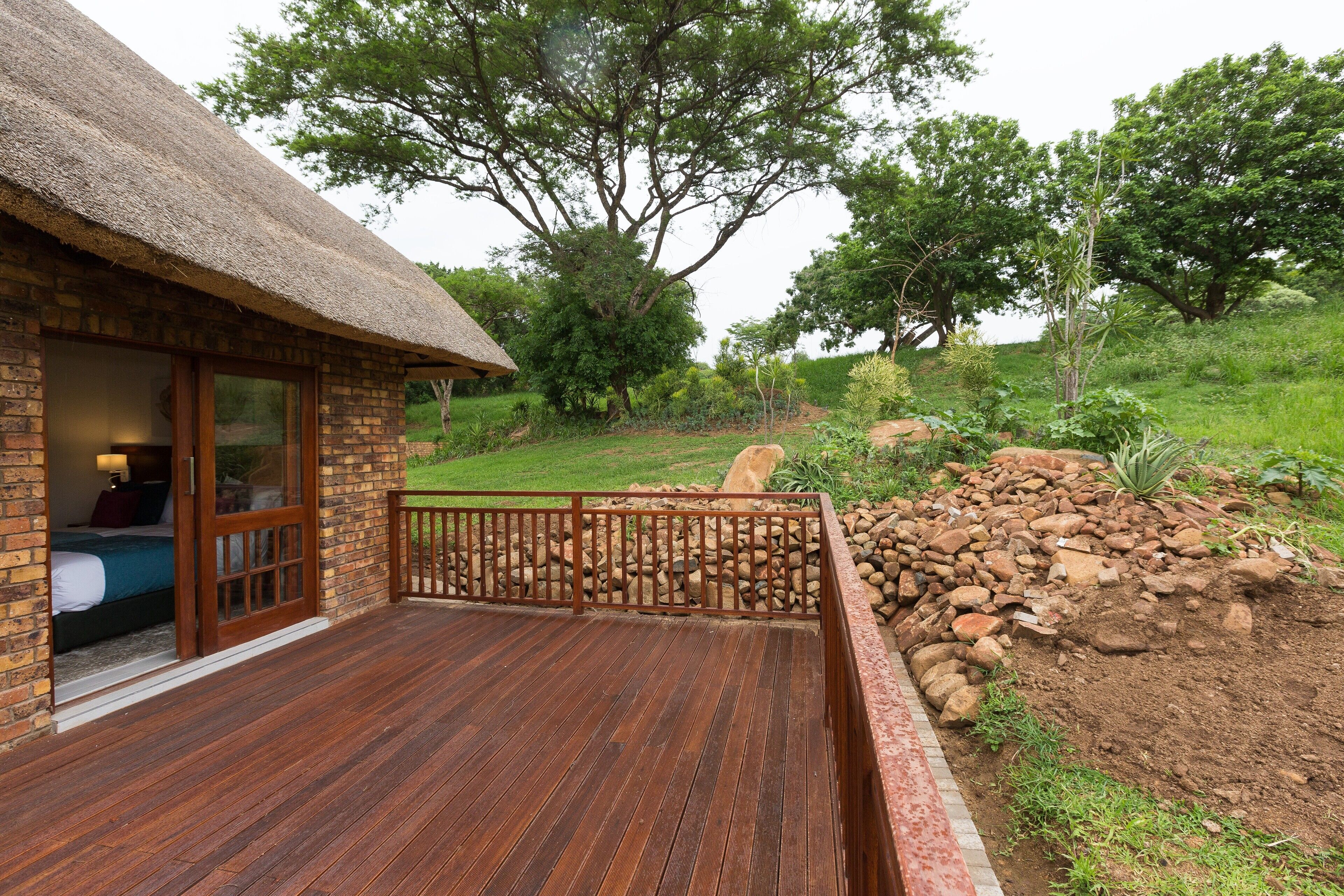 Un chalet rustique avec un toit de chaume, une terrasse en bois et une vue sur un jardin luxuriant et des arbres.