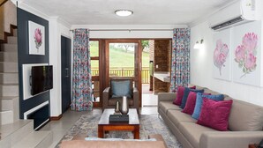 A living room with a sofa, a coffee table, a TV mounted on the wall, and a staircase leading to an outdoor area. - Kruger Park Lodge Unit 608B (Mbombela)