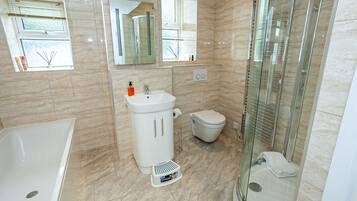 Een moderne badkamer met een badkuip, wastafel, toilet en douchecabine met glazen wanden.