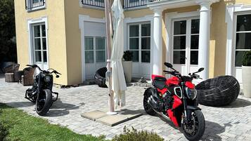Una casa de dos pisos con un camino de entrada pavimentado, dos motocicletas estacionadas afuera y un paraguas blanco.