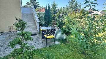 A residential backyard with a paved patio, a small table and chairs, and a variety of plants.