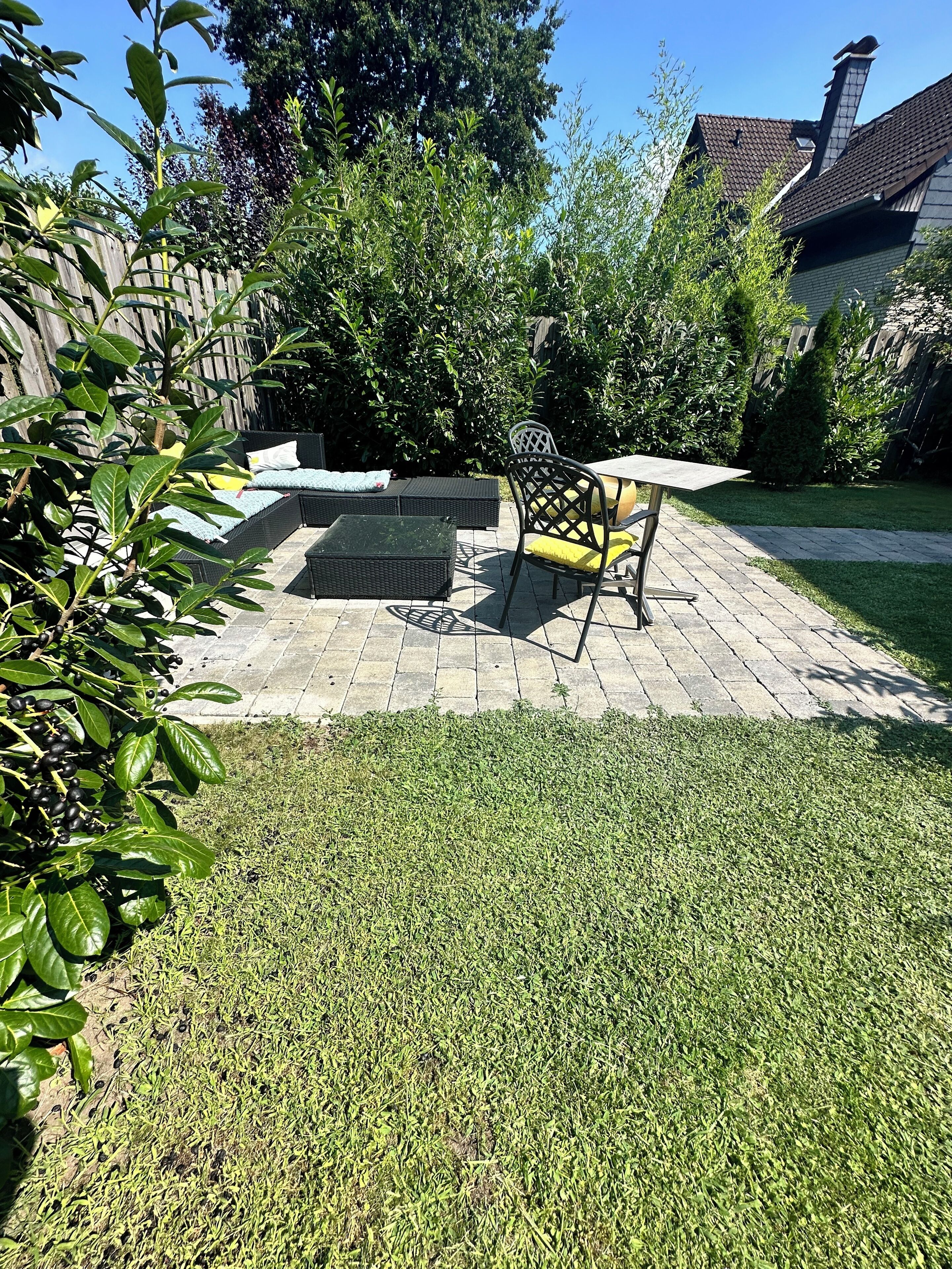 A patio area with a table and chairs, surrounded by a wooden fence and greenery.