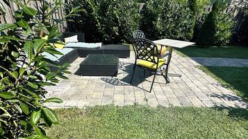 A patio area with a table and chairs, surrounded by a wooden fence and greenery.