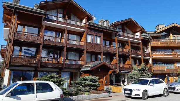 A multi-story wooden building with balconies, a ski lift, and parked cars.