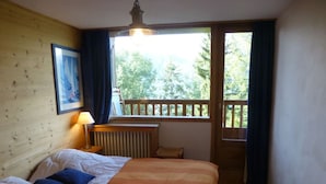 A bedroom with a bed, a window with a view of trees, a radiator, and a picture on the wall.