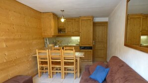 A compact living space with a kitchenette, wooden furniture, and a brown sofa with blue cushions.