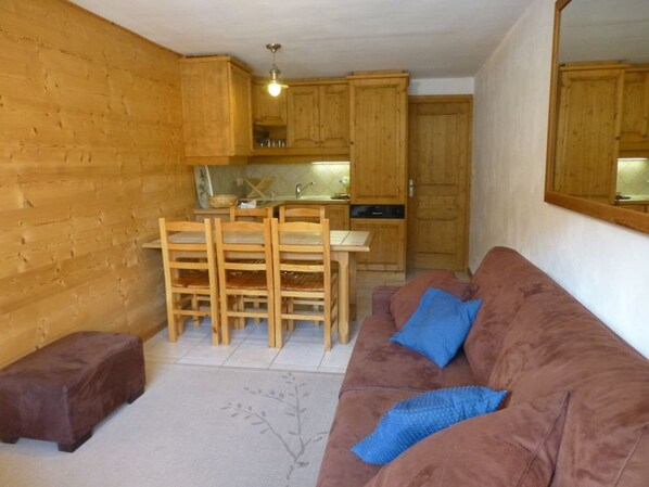 A compact living space with a kitchenette, wooden furniture, and a brown sofa with blue cushions. - Charming 2-room apartment in Courchevel! (Courchevel 1550)