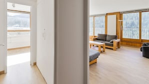 A spacious living area with a sofa, a small table, and a view of a snowy landscape through large windows.
