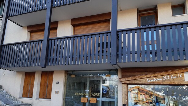 A modern building with a glass entrance, wooden shutters, and a balcony with vertical slats.