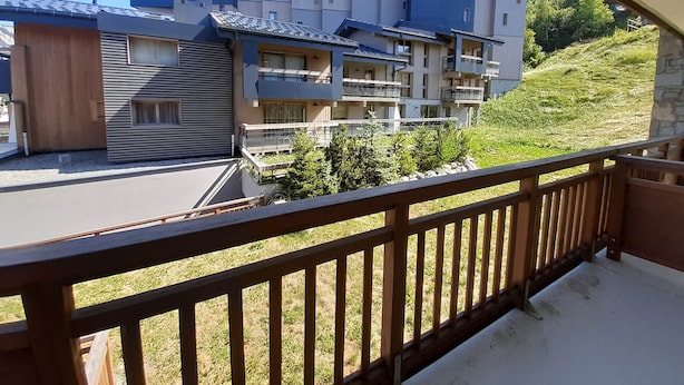 Un moderno edificio de apartamentos con varios balcones, techo plano y vista a una colina verde.