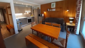 Un espacio habitable pequeño con una mesa de madera, bancos, un sofá y una kitchenette.