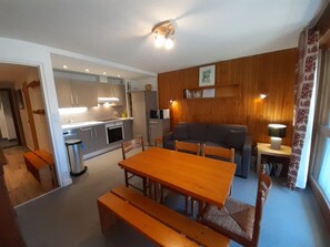 Um espaço compacto com mesa de jantar de madeira, bancos, sofá e pequeno canto para cozinha.