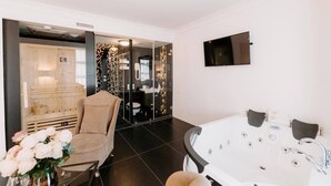 A modern bathroom with a large bathtub, a glass-enclosed shower, and a beige chair. - Golden Hotel (Pristina)