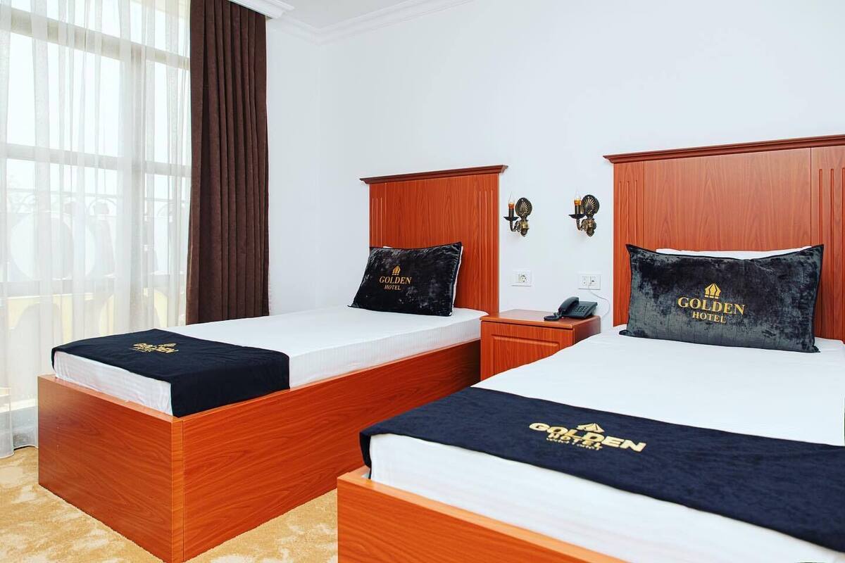 A hotel room with two beds, wooden headboards, a nightstand, a telephone, and a window with curtains.