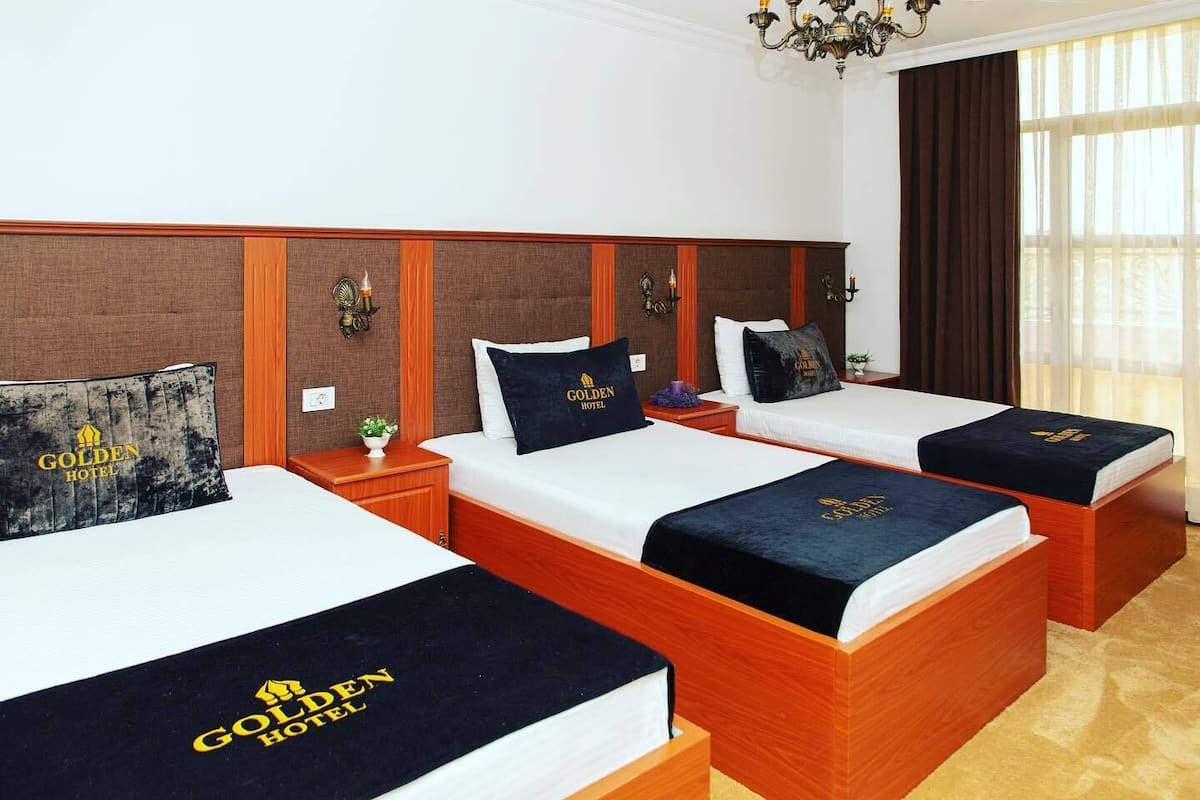 A hotel room with three beds, each with a headboard and a bedspread featuring the hotel's logo.