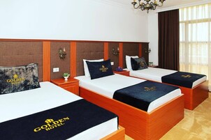Habitación de hotel con tres camas, cada una con cabecera y colcha que muestra el logotipo del hotel.