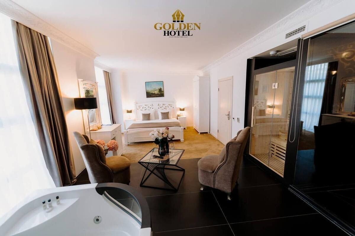 A modern hotel room with a bed, seating area, and a glass partition.
