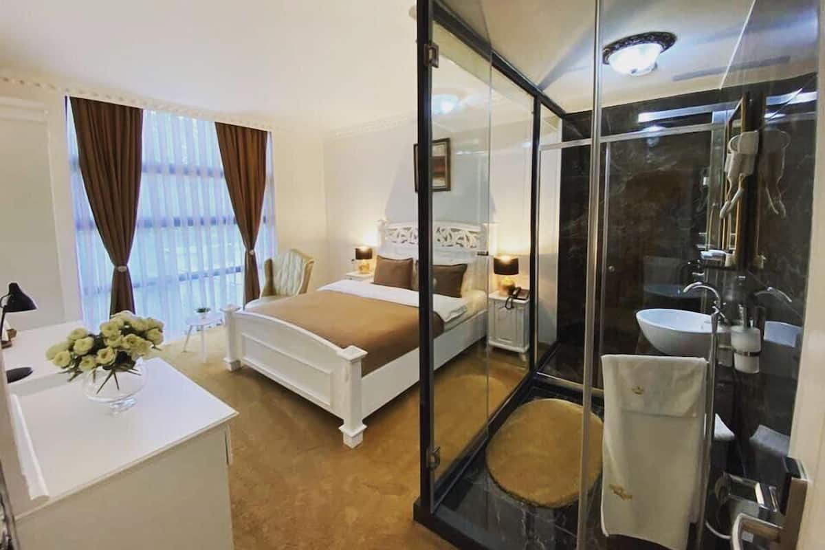 A hotel room with a bed, bedside table, lamp, and a large mirror.