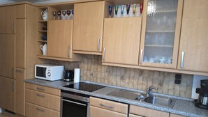 Een keuken met houten kastjes, een magnetron, een koffiezetapparaat en een spoelbak.