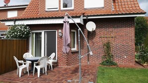 Een tweelaags huis met een bakstenen gevel, een pannendak en een terras met tuinmeubilair.