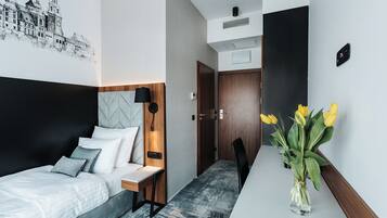 A modern hotel room with a bed, bedside table, lamp, and a vase with flowers.
