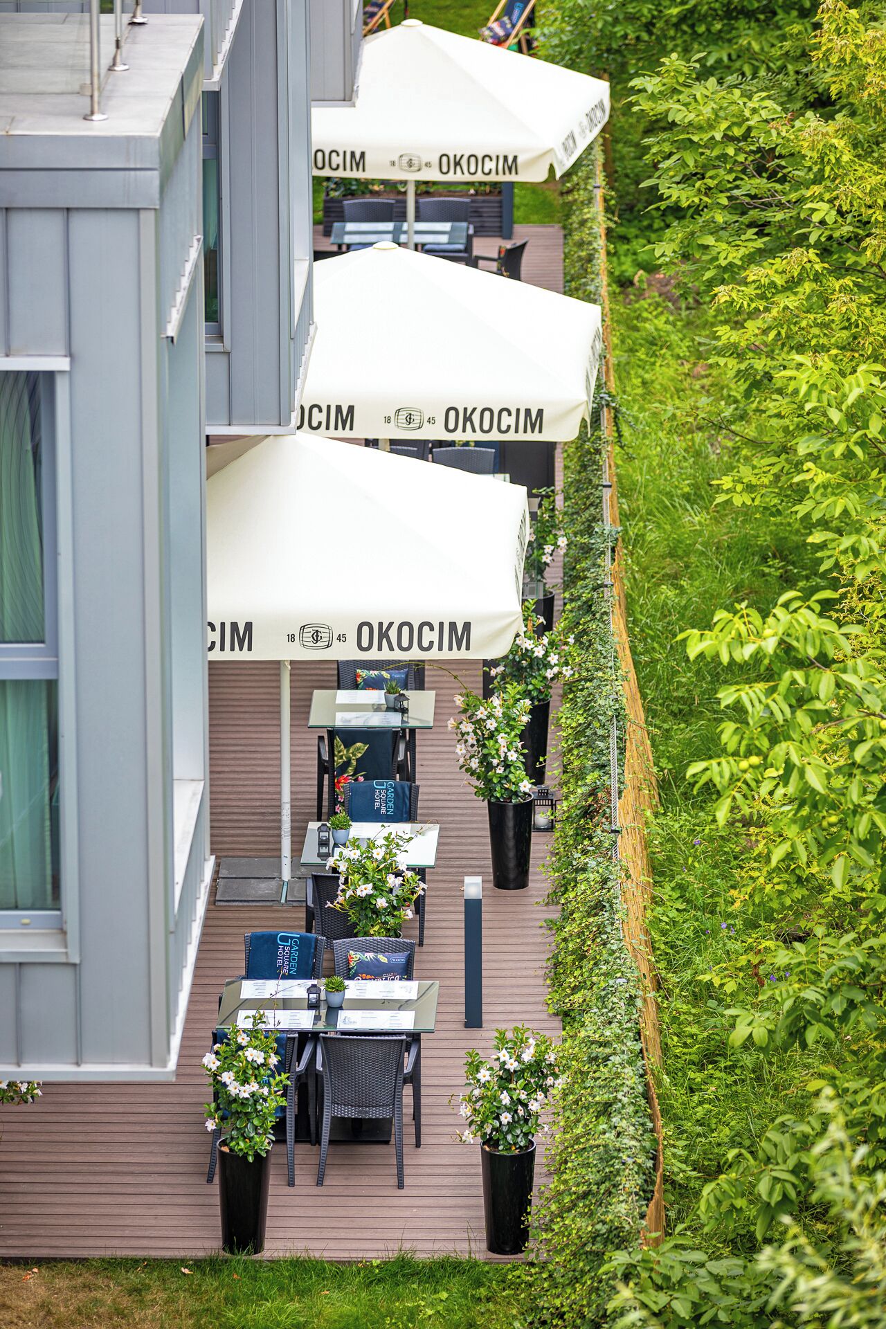 Un espace extérieur moderne, aménagé avec des tables et des chaises, et protégé par des parasols portant l’inscription « OKOCIM ».