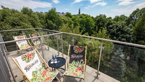 A balcony with two chairs and a table, each with a 'República' banner, overlooking a lush green area with a river and trees. - Focus Hotel Premium Kraków (Kraków)