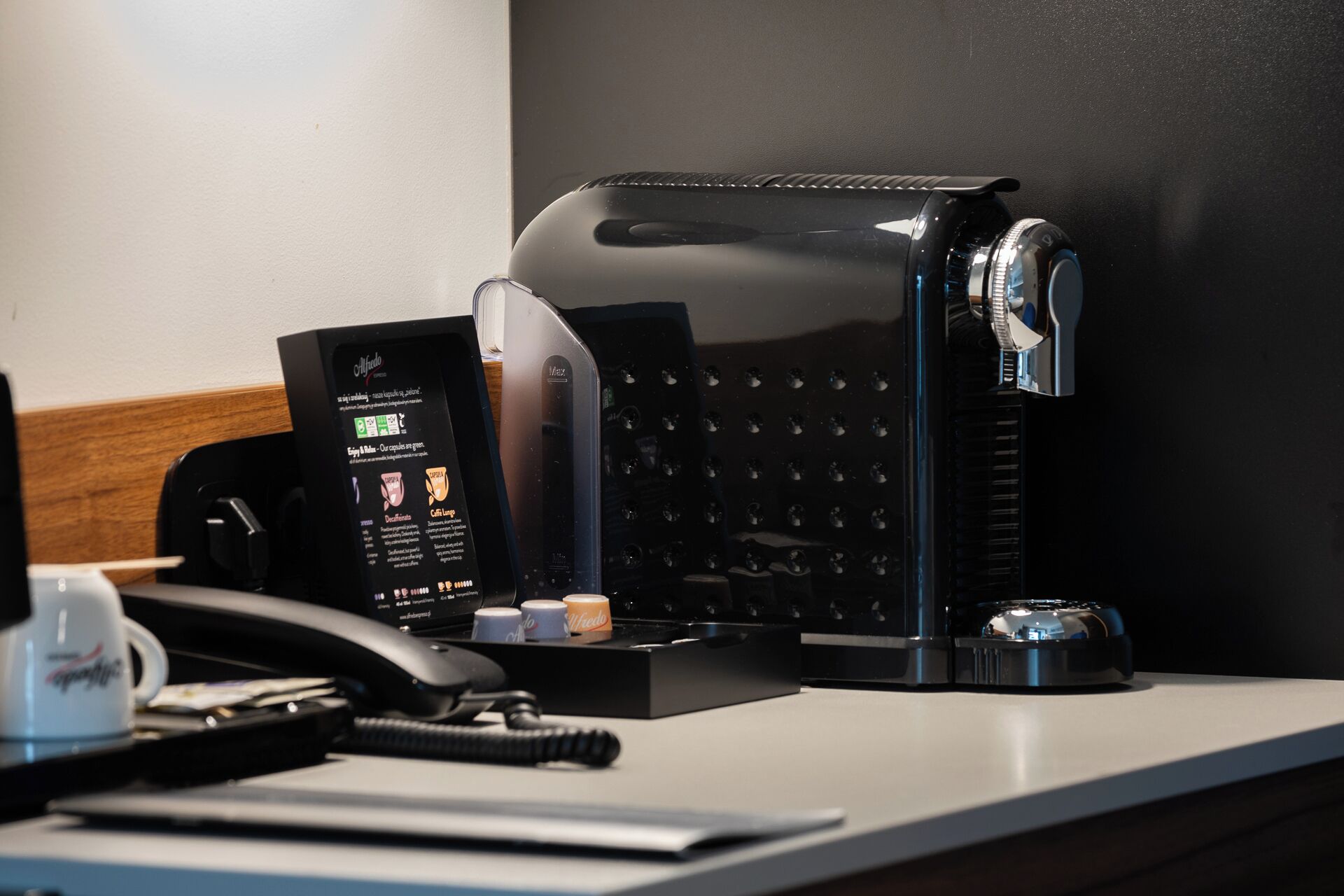 A coffee machine with a digital display, a phone, and a small coffee cup on a counter.