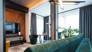 A modern living room with a sofa, a TV, a small table with a bottle, and a plant. - Focus Hotel Premium Kraków (Kraków)