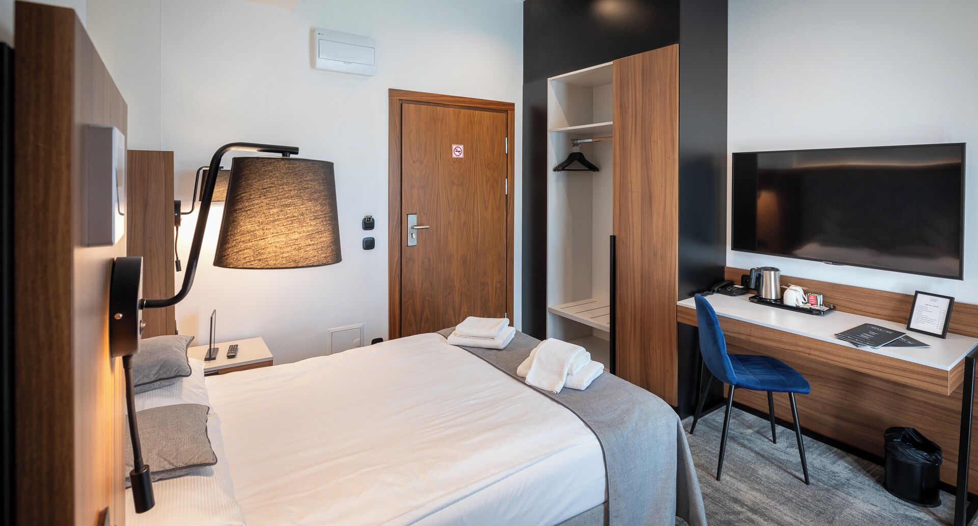 A hotel room with a bed, desk, chair, TV, and a wardrobe.