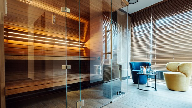 A modern interior with a glass partition, wooden paneling, a blue sofa, a yellow armchair, and a small table with glasses and a candle. - Focus Hotel Premium Kraków (Kraków)