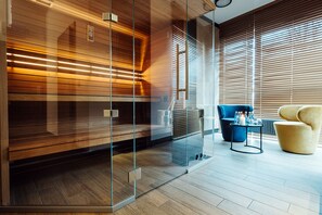 A modern interior with a glass partition, wooden paneling, a blue sofa, a yellow armchair, and a small table with glasses and a candle. - Focus Hotel Premium Kraków (Kraków)