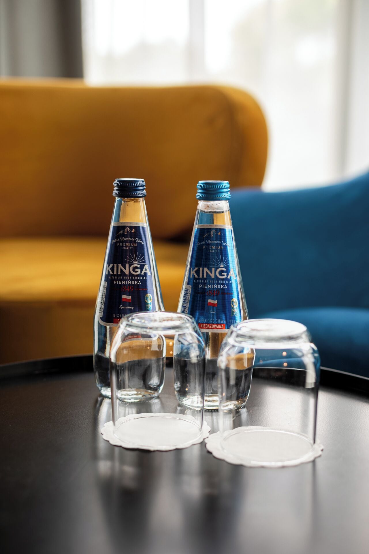 Two bottles of Kinga premium vodka and three empty glasses on a table.