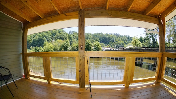 Een houten terras met een hekwerk, met uitzicht op een waterpartij en een beboste heuvel.