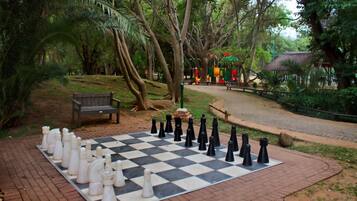 A chessboard set up outdoors with trees and a bench in the background.