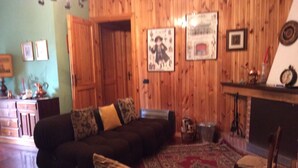 A cozy living room with a dark brown sofa, patterned cushions, a red and beige rug, and wooden walls.
