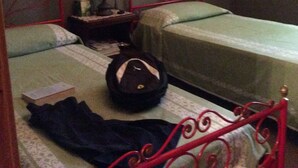 A room with two single beds, a nightstand with a lamp, a suitcase, and a framed picture on the wall.