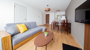 Uma sala de estar moderna com um sofá cinza, mesa de centro de madeira e um espaço de jantar com cadeiras e mesa de madeira.